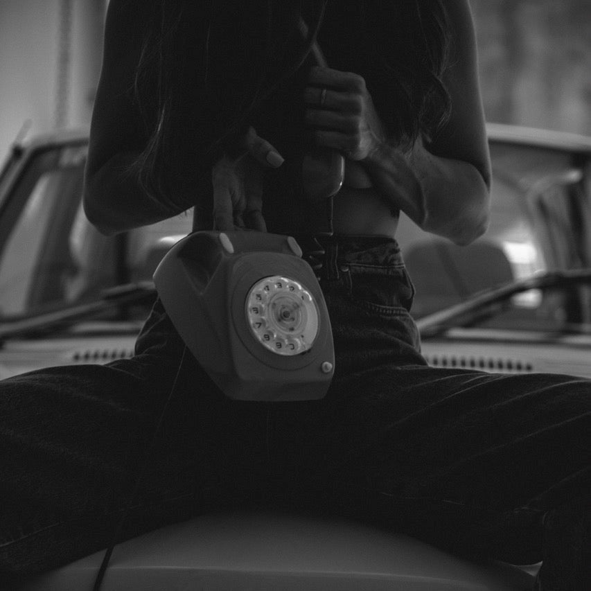 Person holding a vintage rotary phone on a car grille with a blurred background