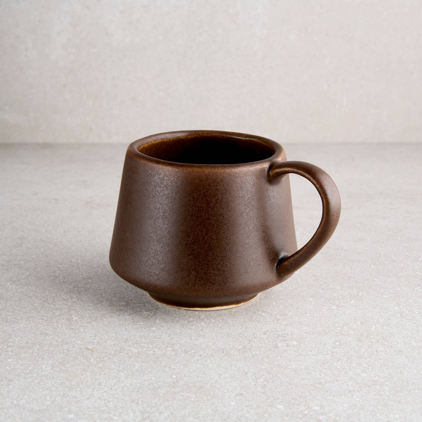 Brown ceramic mug on a light gray surface with a neutral background
