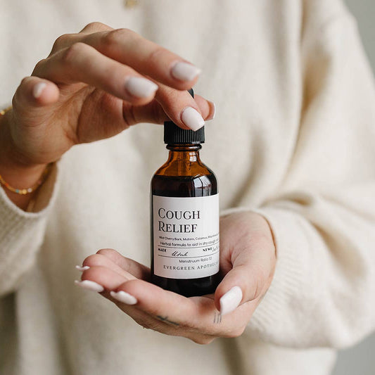 Person holding a bottle labeled 'Cough Relief' by Evergreen Apothecary.